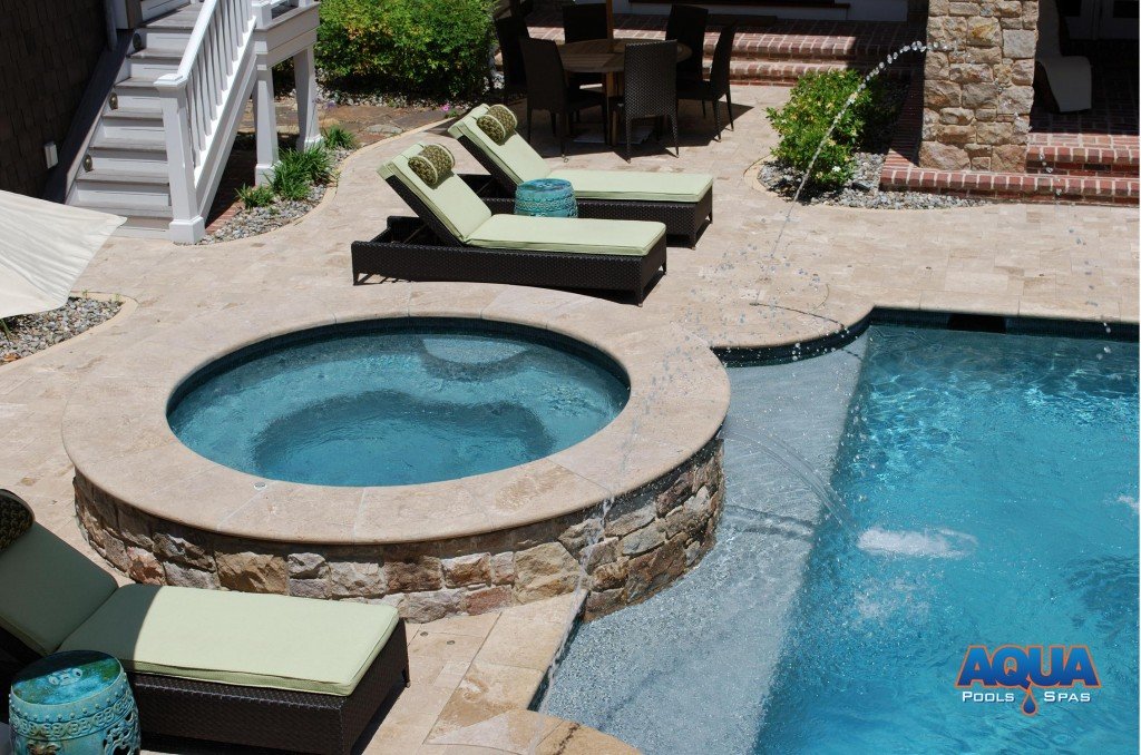 Instead of having a "spill over" into the pool which would dictate the bodies of water (& heat) be shared, we recommend separating the bodies of water. A waterfall of recirculated pool water can be added to the face of the hot tub to achieve the spillover effect without sharing the water.
