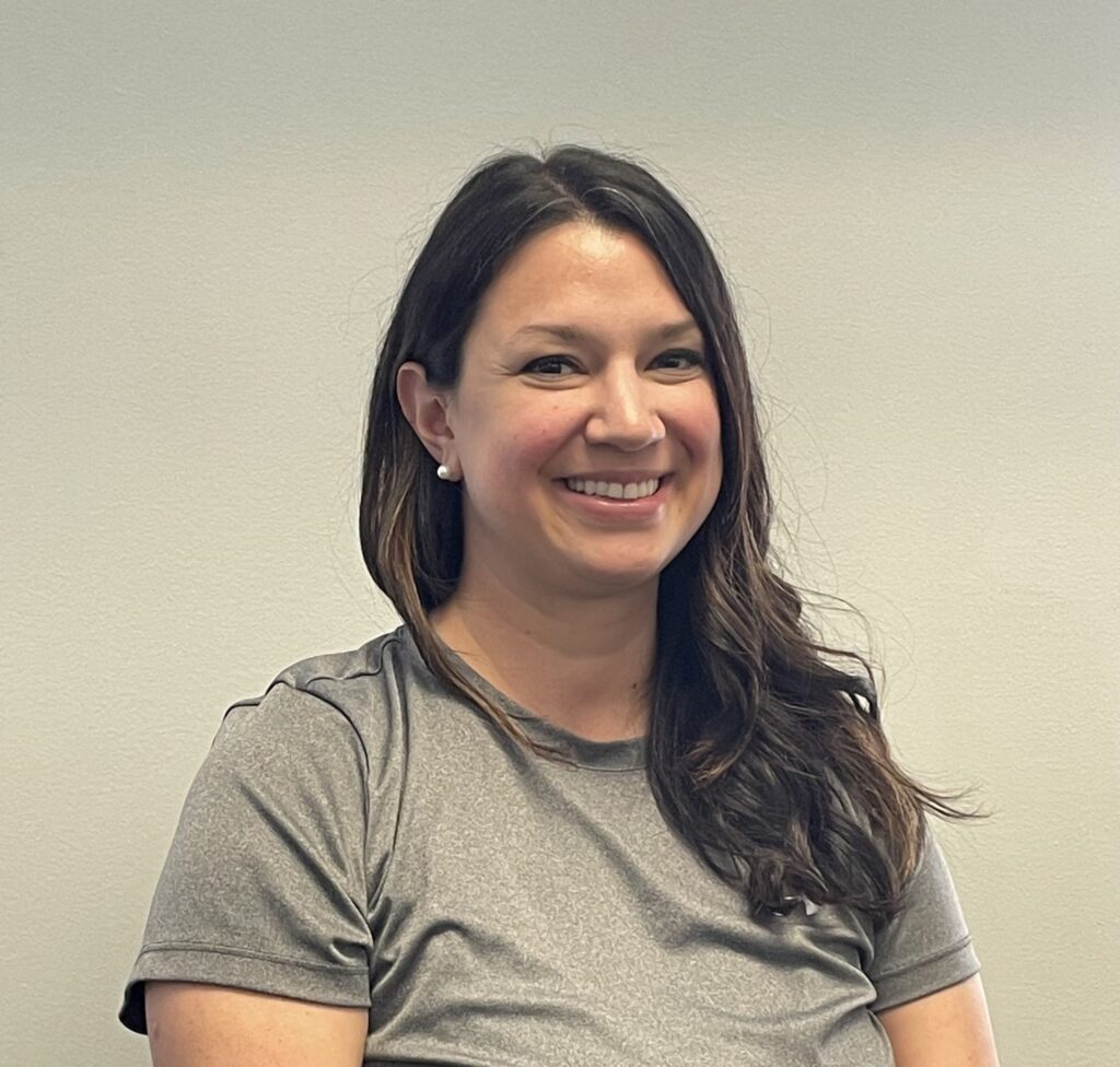 a smiling woman in a gray shirt holding a cell phone
