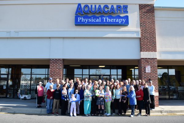 Group of people gathered outside Aquacare Physical Therapy in Millville, Delaware, celebrating the clinic's opening, with the clinic's sign prominently displayed.