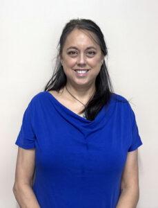 a woman in a blue shirt is standing in front of a white wall