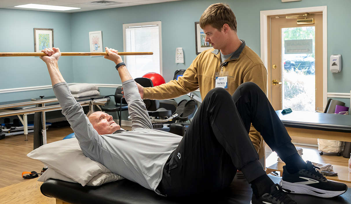 Physical Therapy for Back Pain man on table raising bar with physical therapist