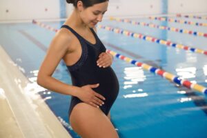 a pregnant woman in a black swimsuit standing next to a swimming pool