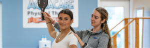 physical therapist working with young woman holding pickleball paddle.