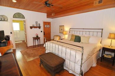 The Gardner’s Cottage Bedroom Atlantic Hotel cottage bedroom with iron bed white comforter harwood floors with table dresser and entrance to bathroom