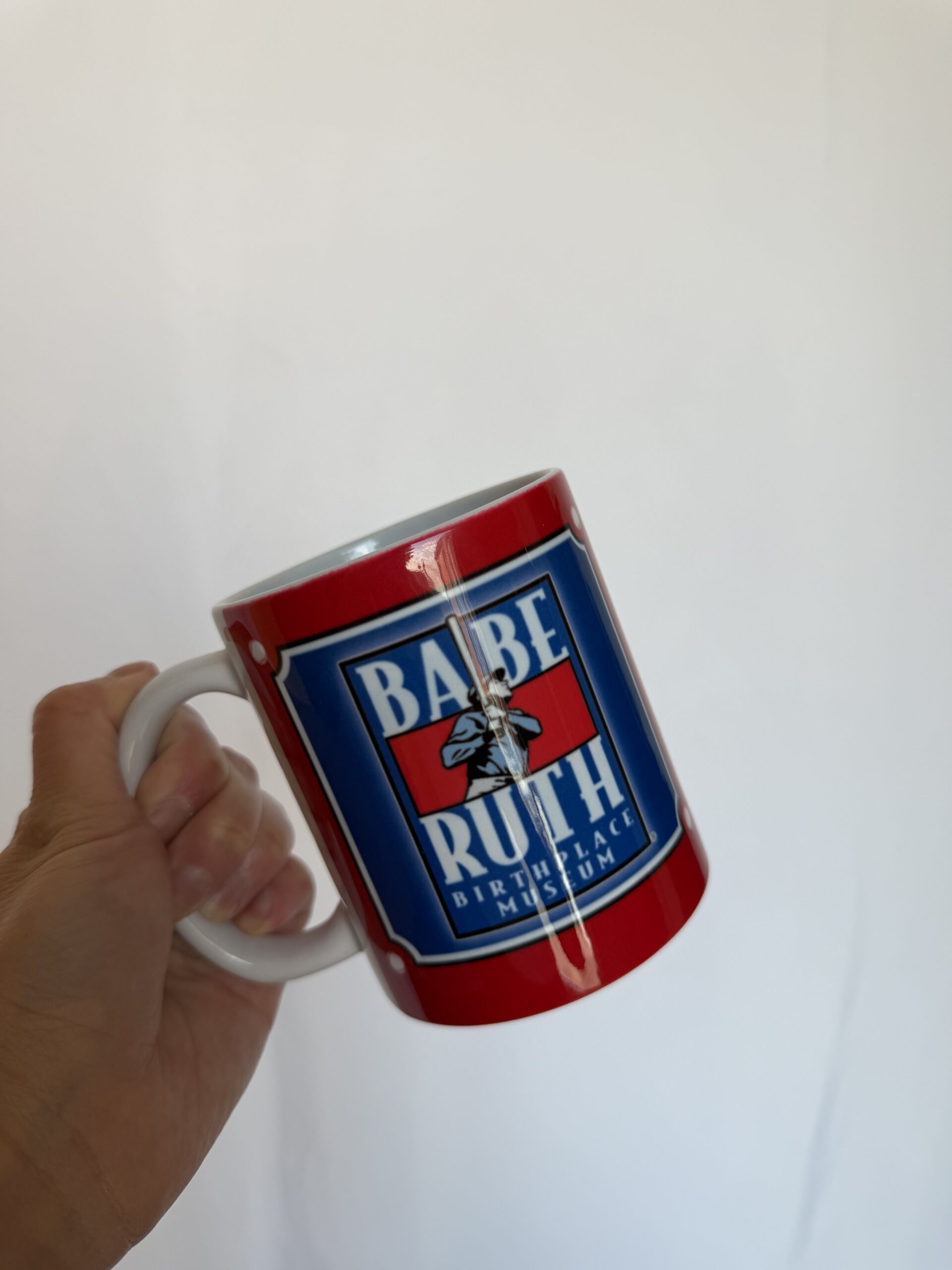 A hand holding the babe ruth museum mug showing the museum's logo