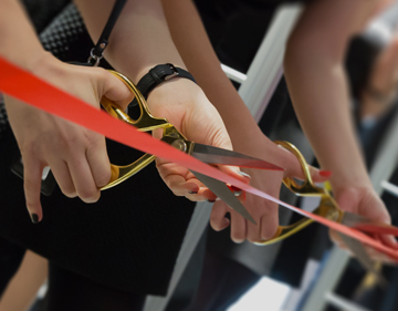 Female using gold scissors to cut a red ribbon