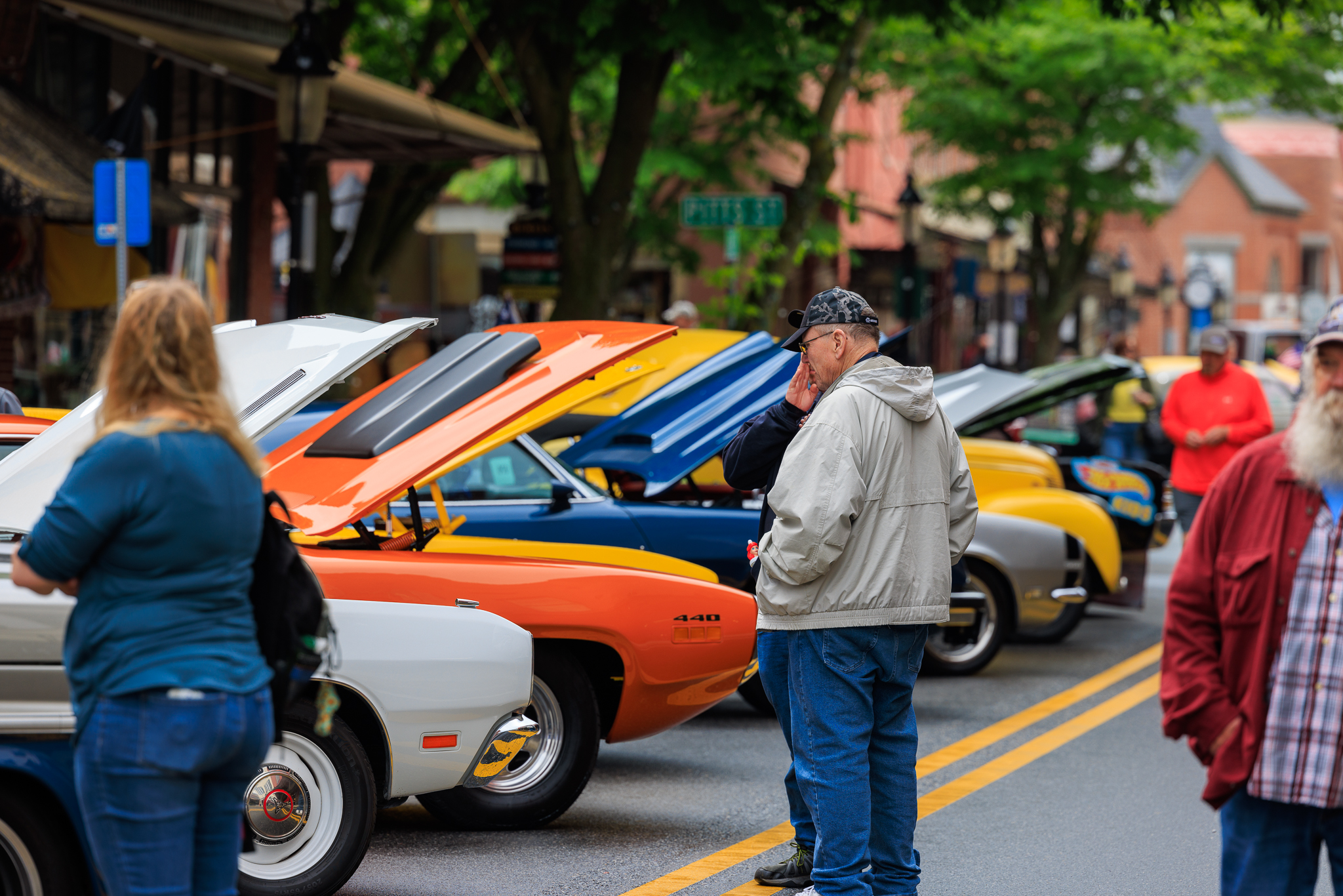 a group of people walking down a street next to parked cars