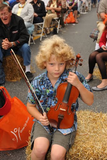 a young boy playing a violin while sitting on hay