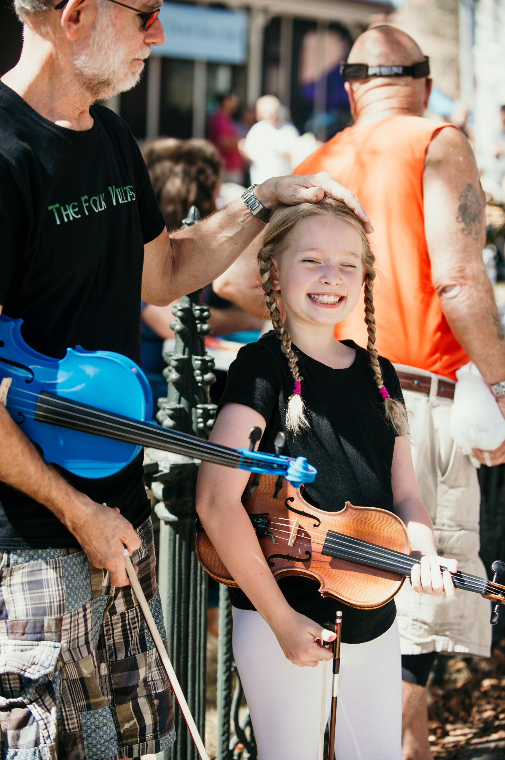 a little girl standing next to a man holding a violin
