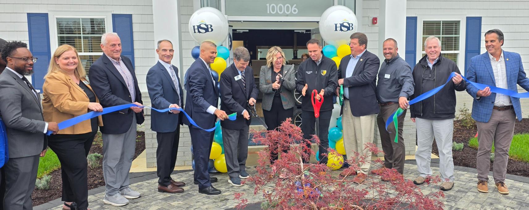 a group of people cutting a ribbon in front of a building