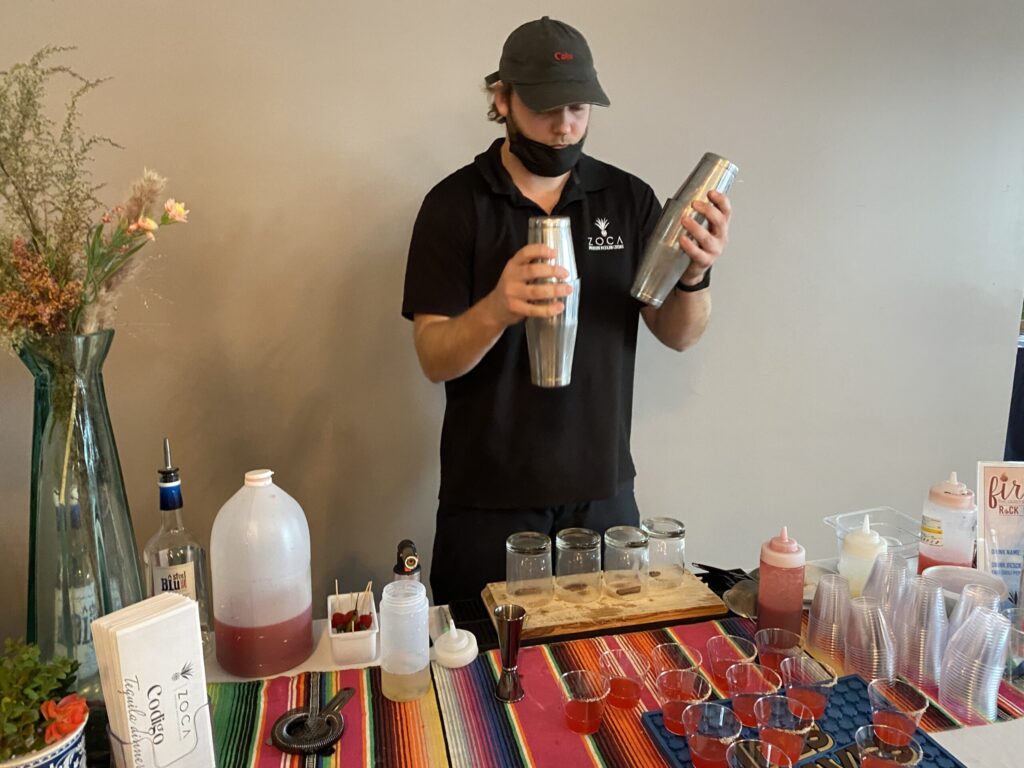 a man standing behind a table with bottles and a blender