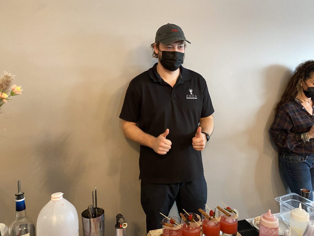 a man wearing a face mask standing in front of a table of drinks