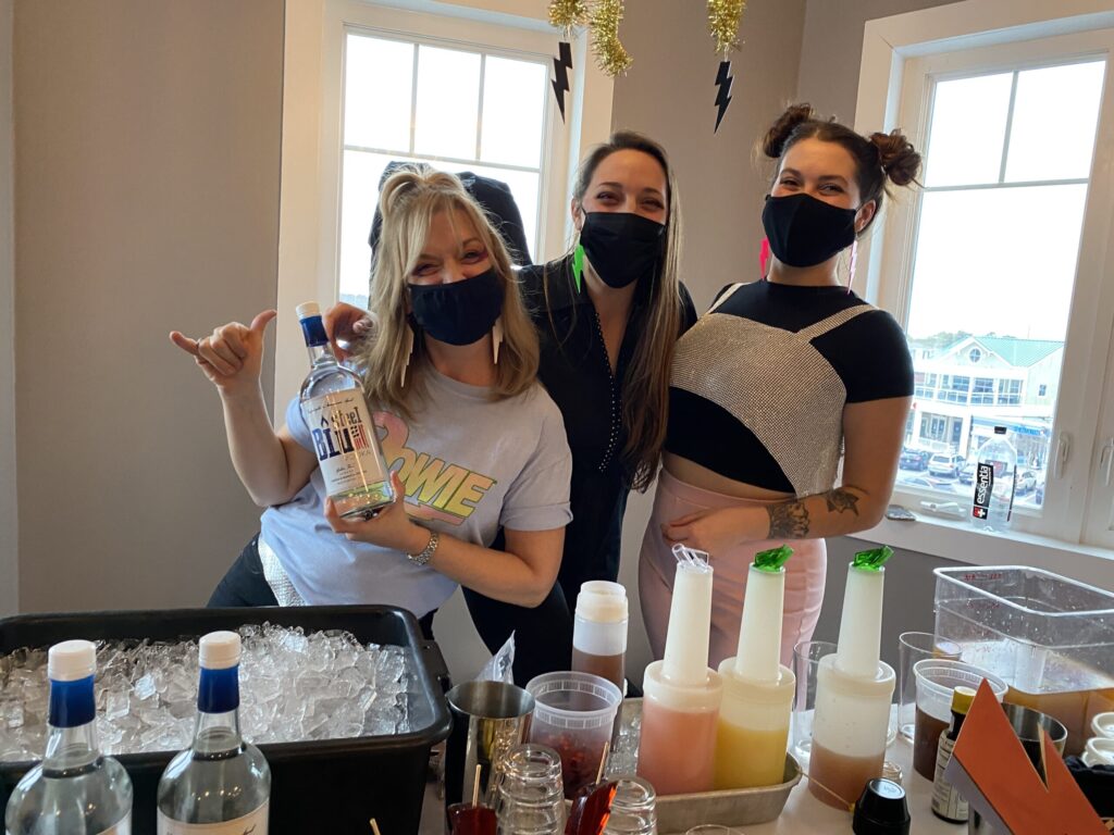 a group of people standing around a table with bottles of alcohol
