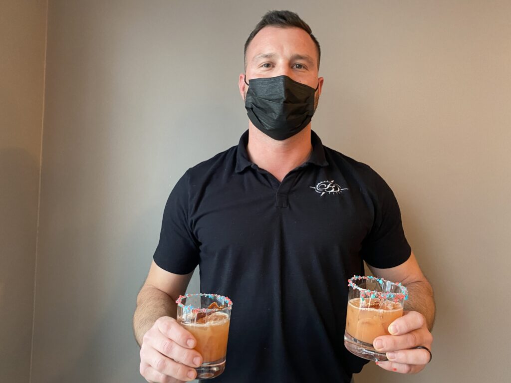 a man wearing a face mask holding two glasses of drinks