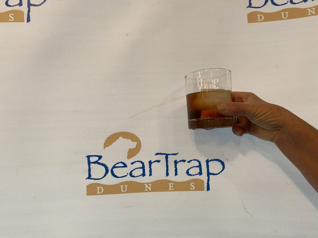 a person holding a glass of beer in front of a sign