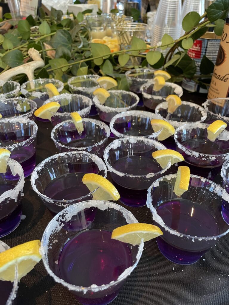 a table topped with glasses filled with purple liquid and lemon wedges