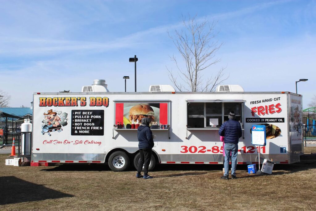 a food truck parked in a field with people standing around it