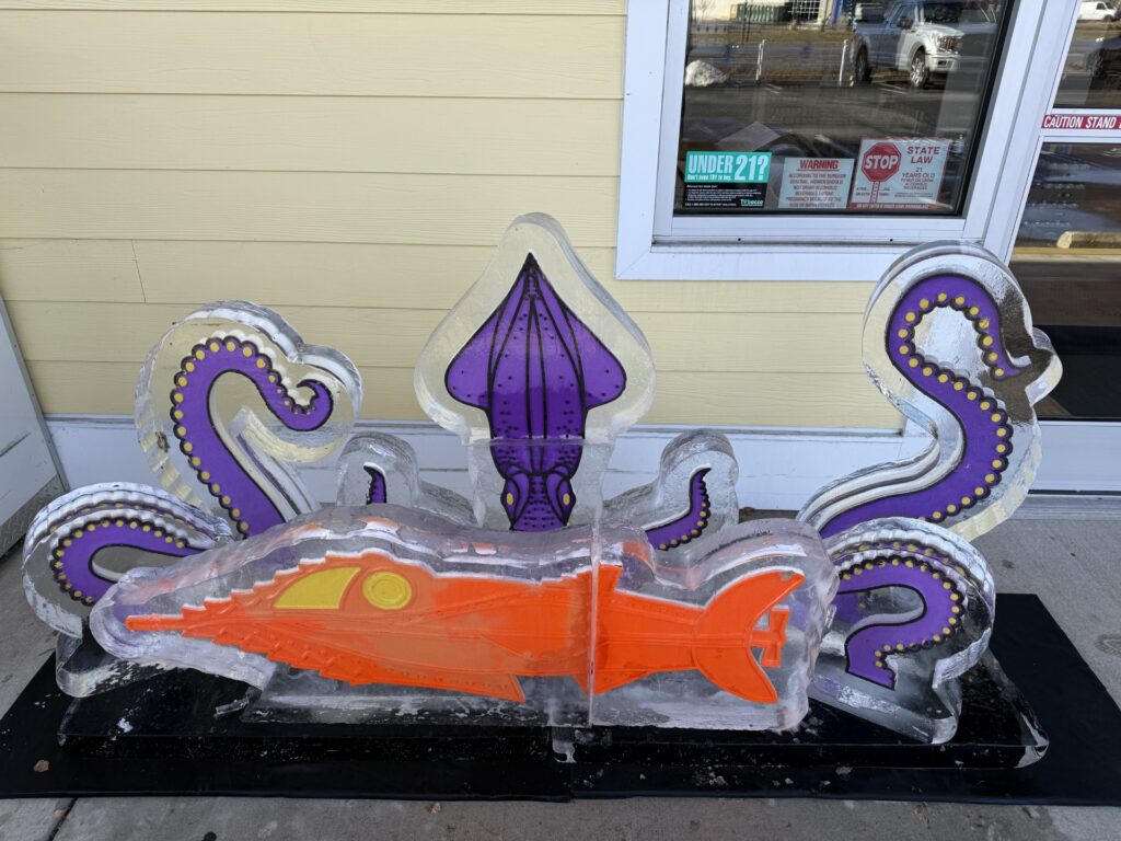 a sculpture of an orange and purple fish in front of a building