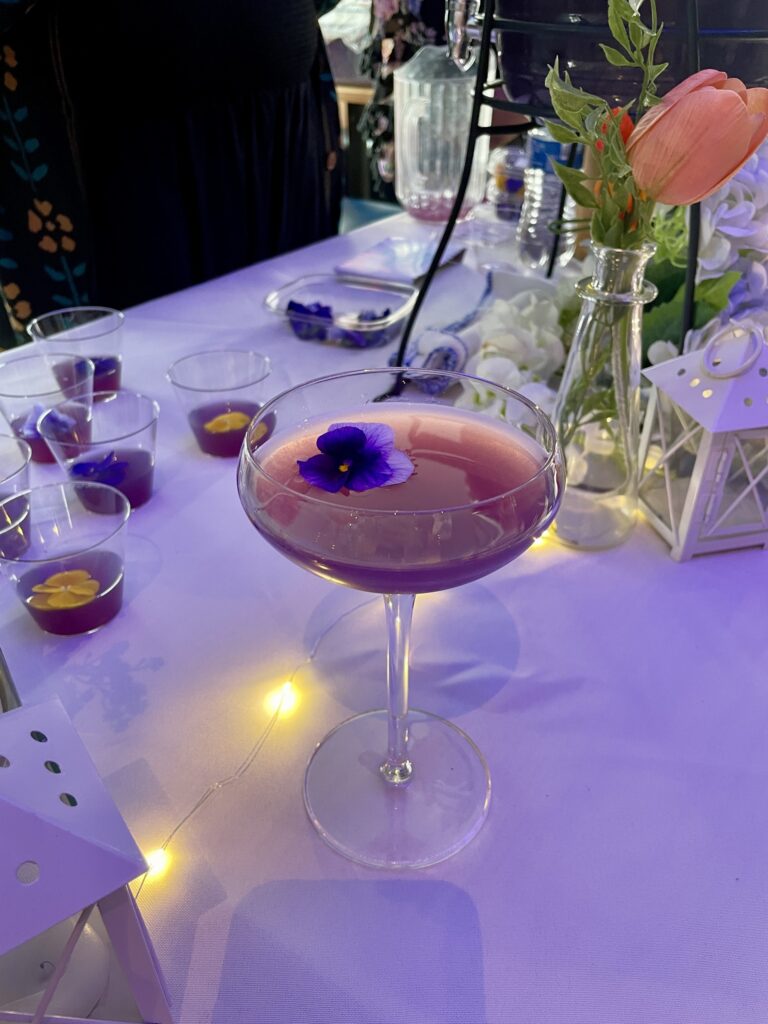a table topped with a purple drink and a vase filled with flowers