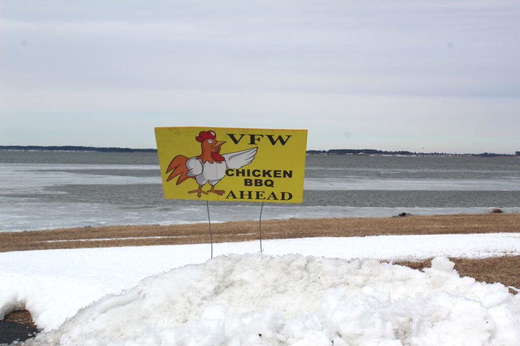 a chicken bbq sign in the snow by the water