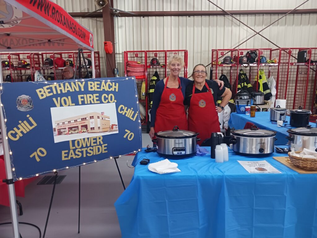 two women in red aprons stand behind a blue table
