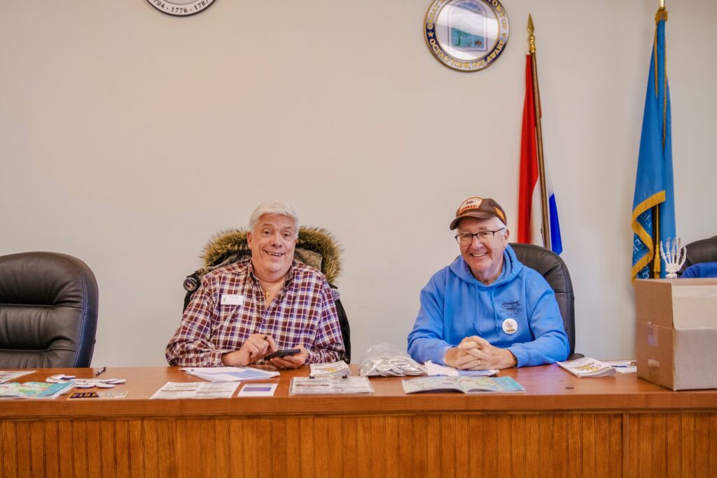 two men sitting at a desk in front of flags