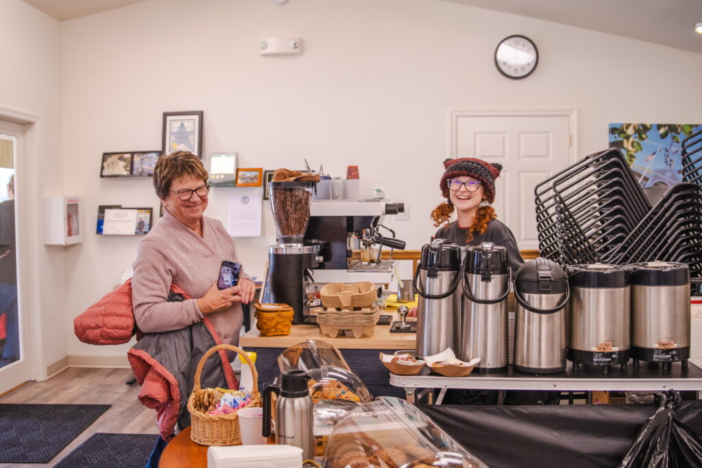 a woman standing behind a counter filled with food