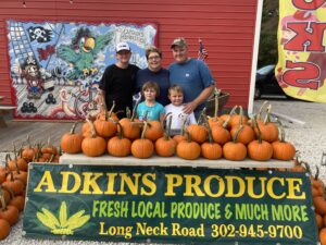 a group of people standing next to a pile of pumpkins