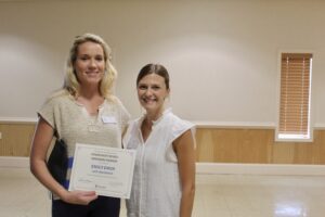 two women standing next to each other holding a plaque