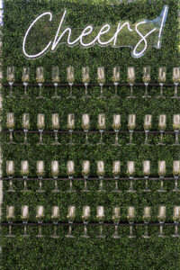 a sign that says cheers on top of a wall of wine glasses