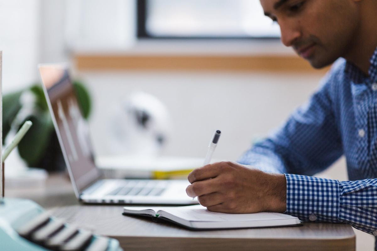 a man sitting at a desk writing on a notebook