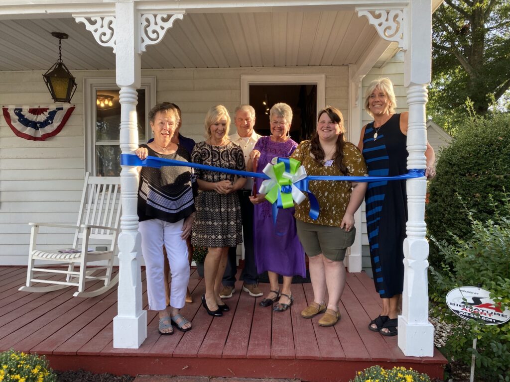 a group of women standing on a porch holding a ribbon