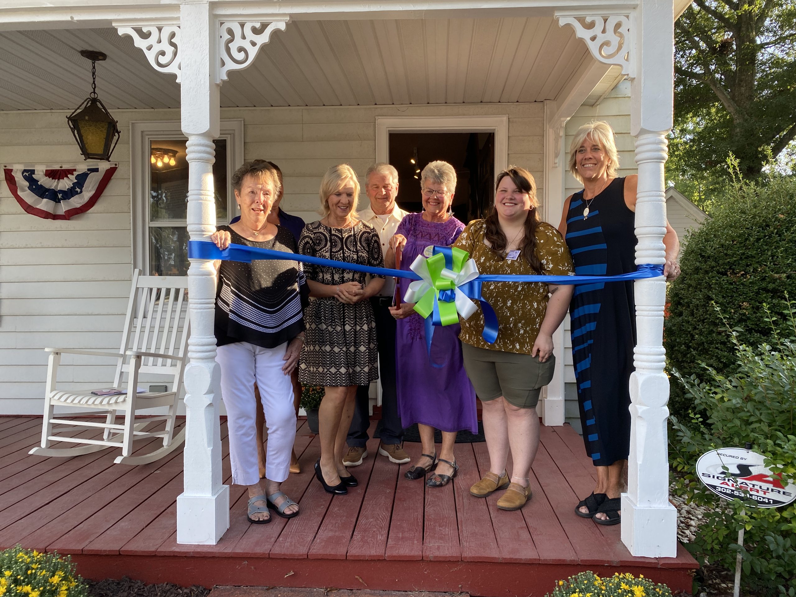 a group of women standing on a porch holding a ribbon