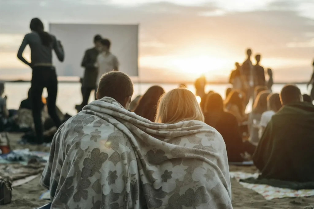 a group of people sitting on the beach watching a movie