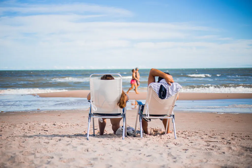 a couple of people sitting in lawn chairs on a beach