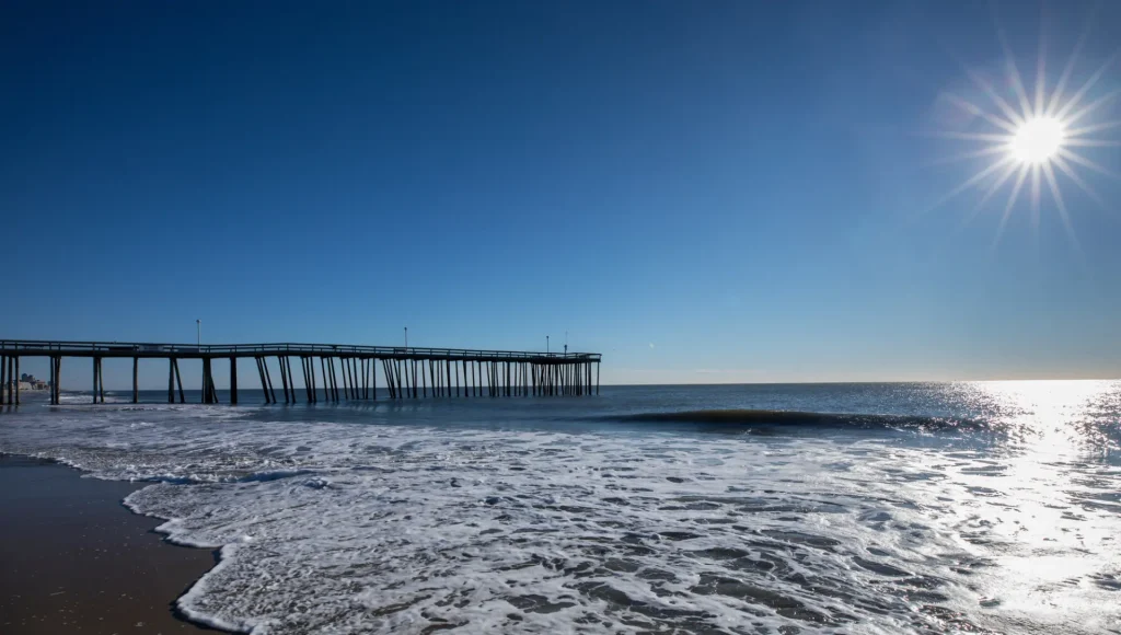 the sun is shining over the ocean and a pier