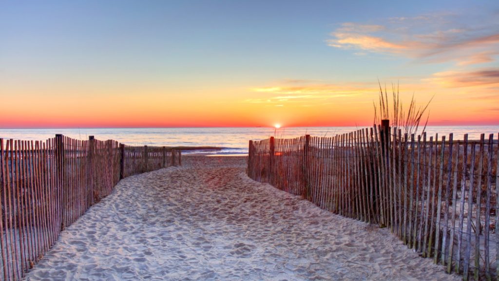 a path leading to the beach with a sunset in the background