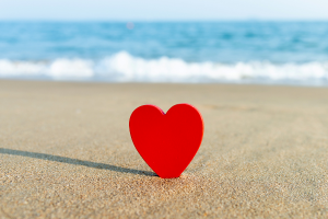 a red heart sitting on top of a sandy beach