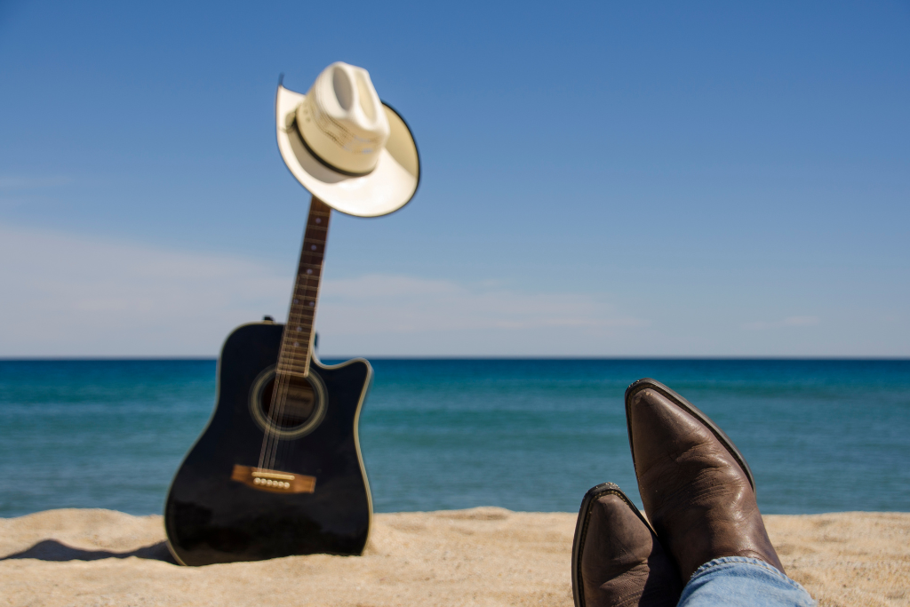 a guitar and a cowboy hat on a beach