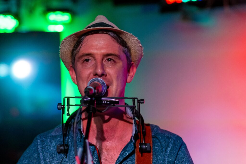 a man with a hat on singing into a microphone