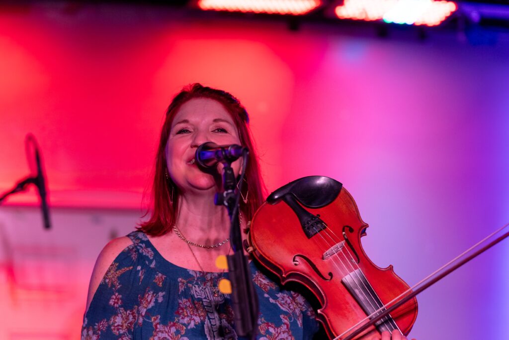 a woman holding a violin and singing into a microphone