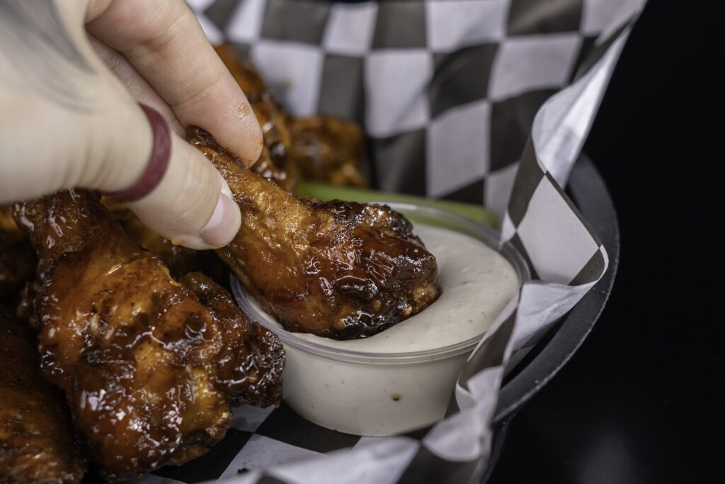 a person dipping sauce on some chicken wings