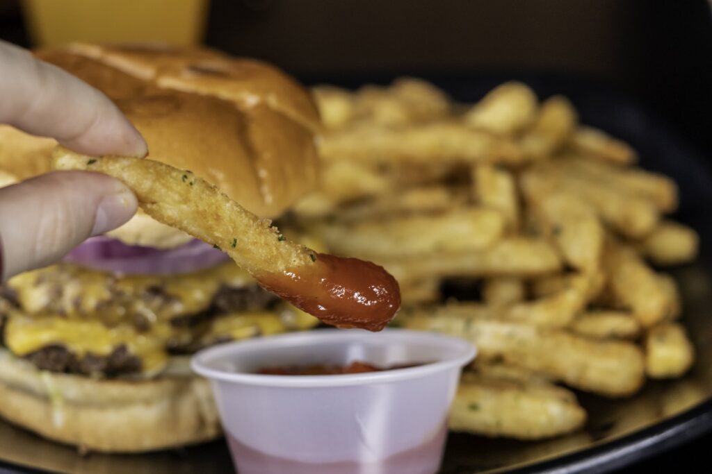 a hand holding a piece of bread over a hamburger