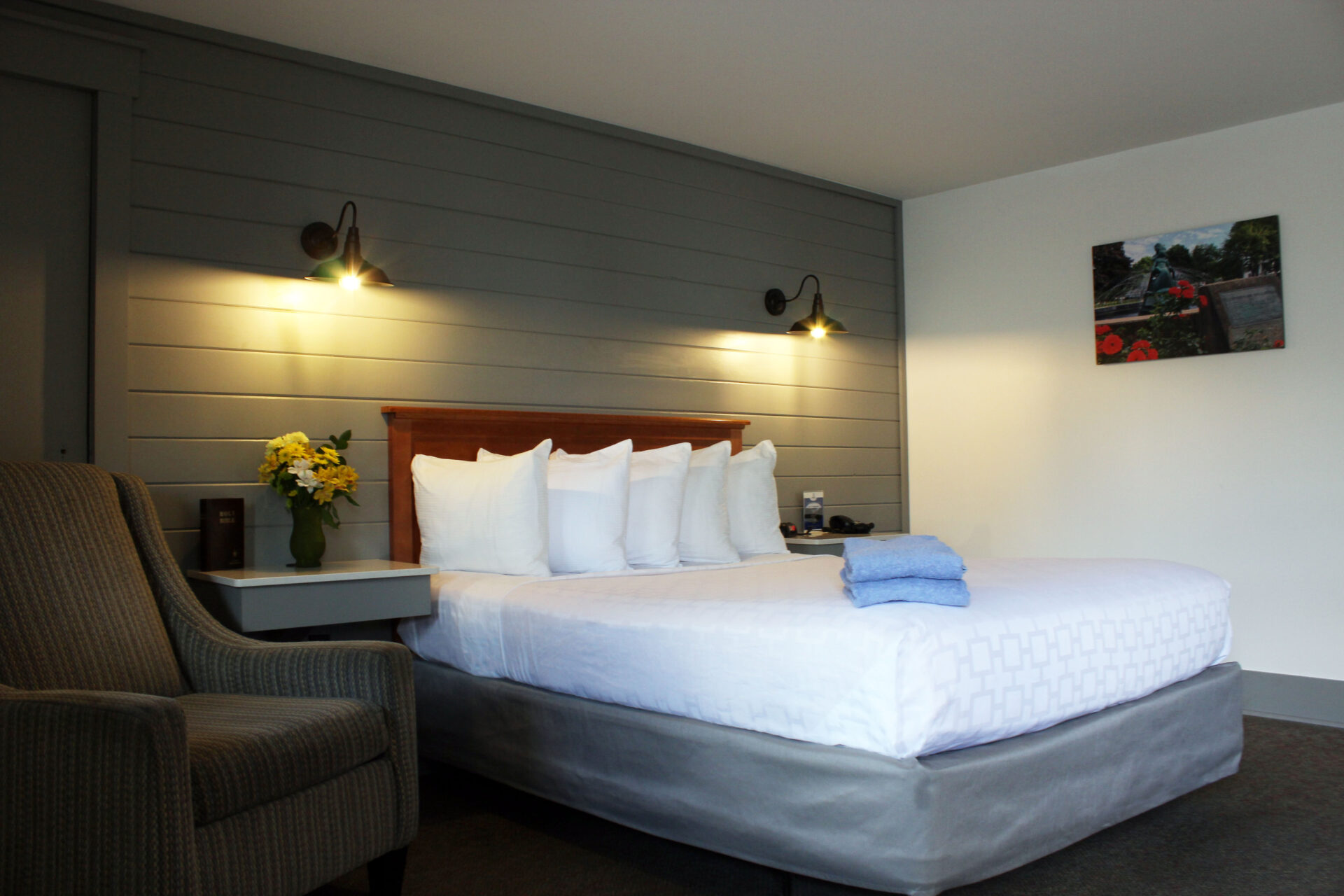 Bed made with white bed sheets with a vase of flowers next to it