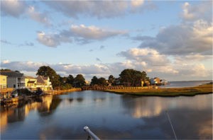 waterfront homes reflected in bay waters under partly cloudy sky at sunset
