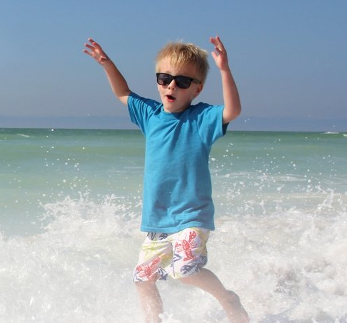 a young boy is standing in the water at the beach
