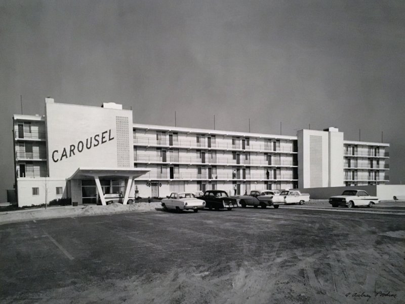 a black and white photo of cars parked in front of a hotel