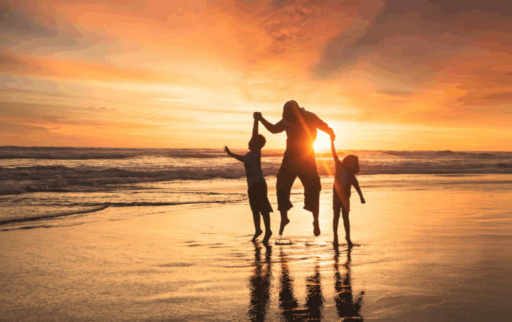 a woman and two children playing on the beach at sunset