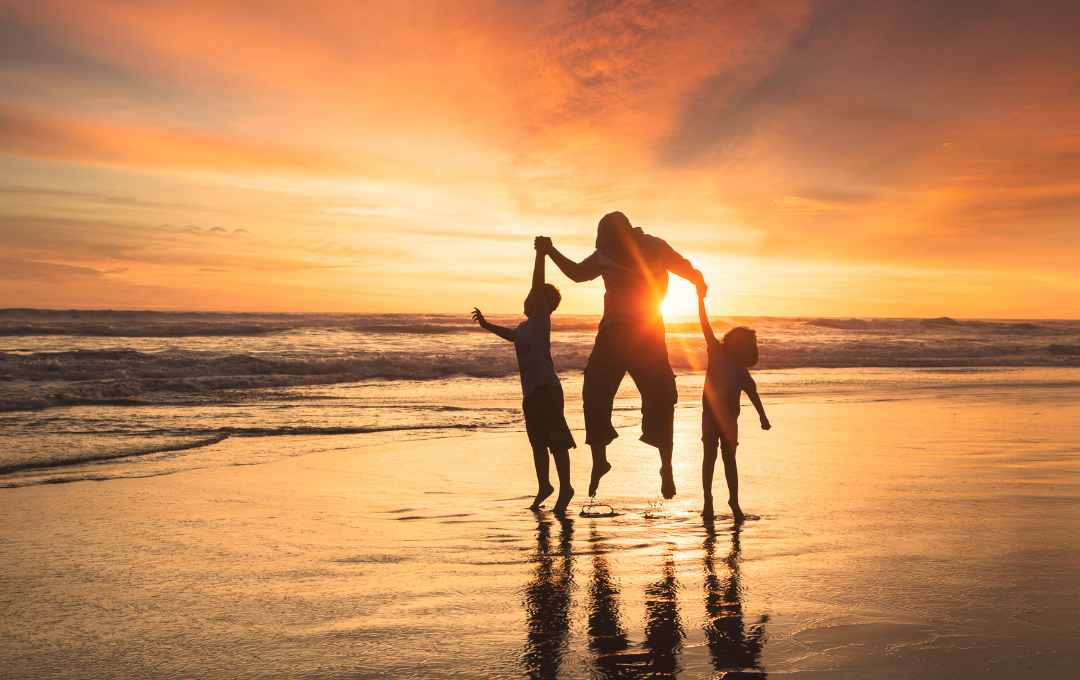 a woman and two children playing on the beach at sunset