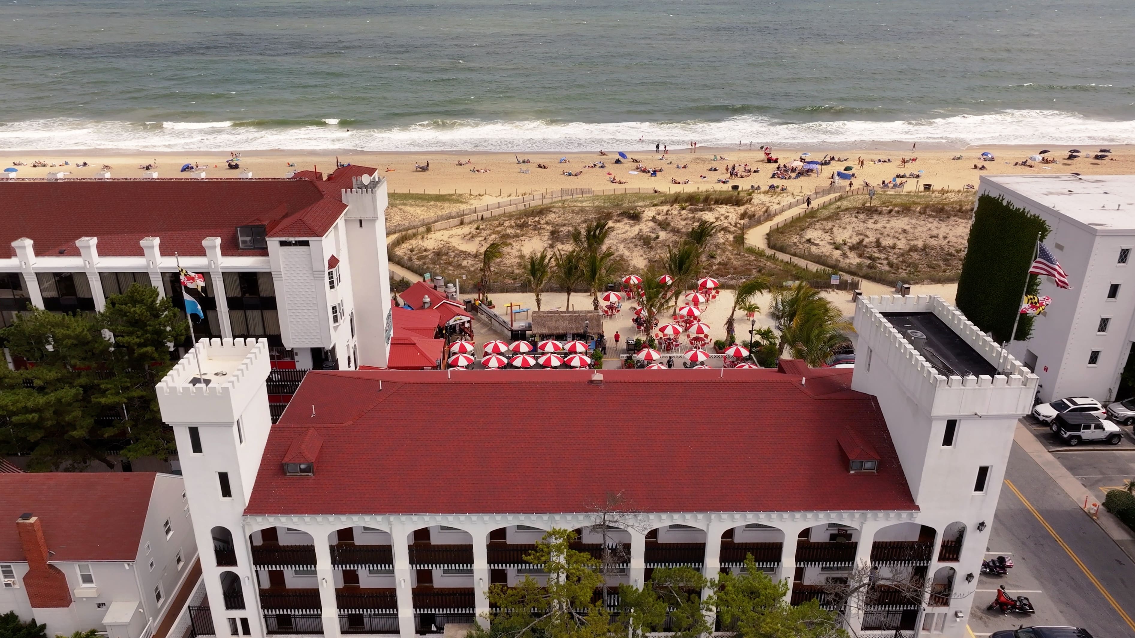 Aerial view of a white building with red roof and beach in the background